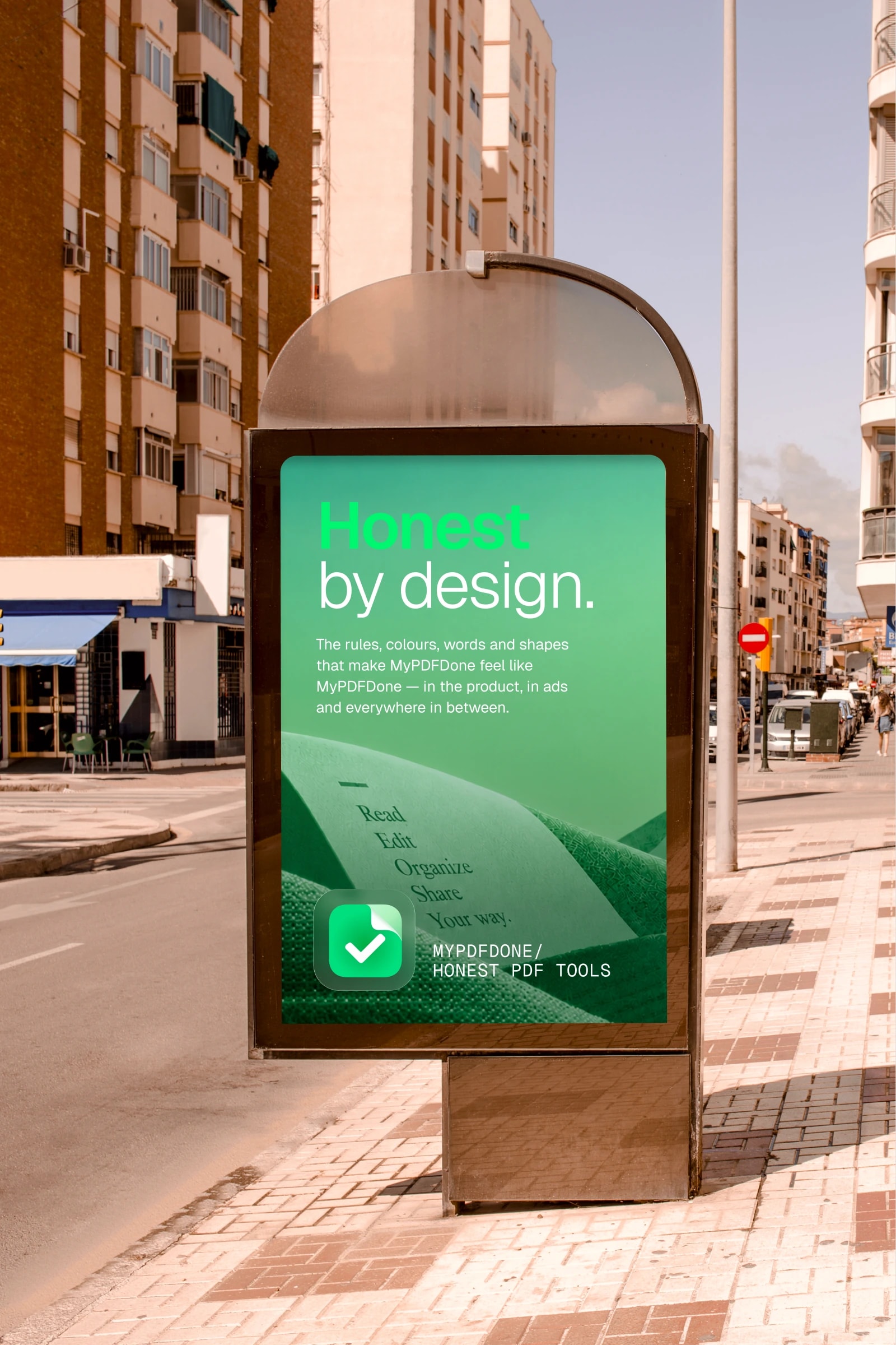 A MyPDFDone poster in a bus shelter on a sunny street: Honest by design. over green paper hills printed with Read, Edit, Organize, Share, and the mark with MyPDFDone / Honest PDF tools